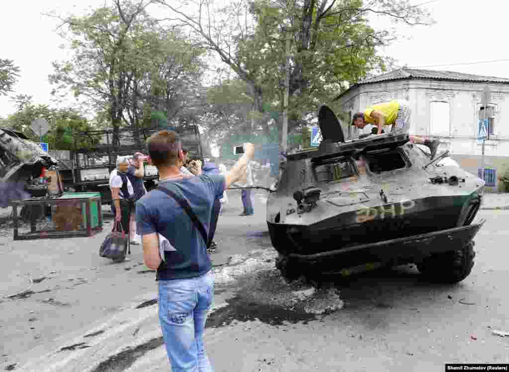 Местные жители фотографируют уничтоженный бронетранспортёр, который принадлежал контролируемым Россией силам, захватившим в городе административные здания. Мариуполь, 13 июня