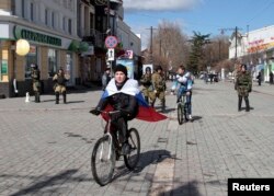 Мальчик с российским флагом на плечах едет на велосипеде. Город Симферополь, 17 марта 2014 года.