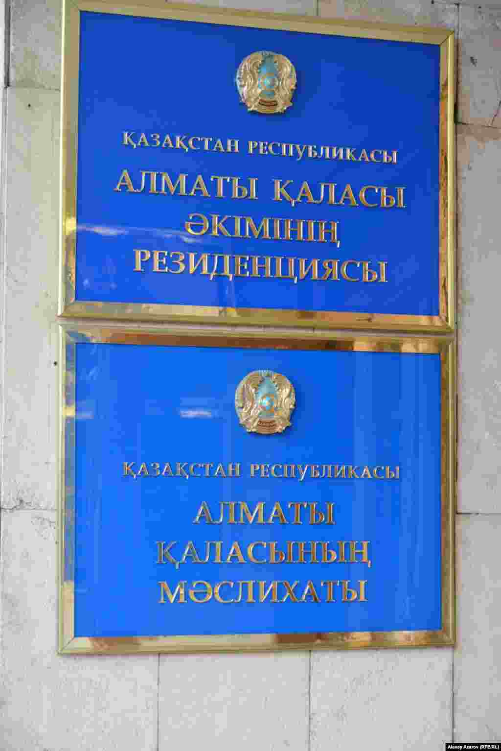 Но если гербов таких больших размеров, как над городским акиматом, в Алматы не так много, то количество подобных табличек с названием государственных учреждений&nbsp;&mdash; огромное число (подразделения акимата, школы, детские сады, поликлиники, больницы и так далее). На каждой вывеске&nbsp;&mdash; изображение герба. И едва ли все они уже заменены на новые, на которых Казахстан пишется как QAZAQSTAN.